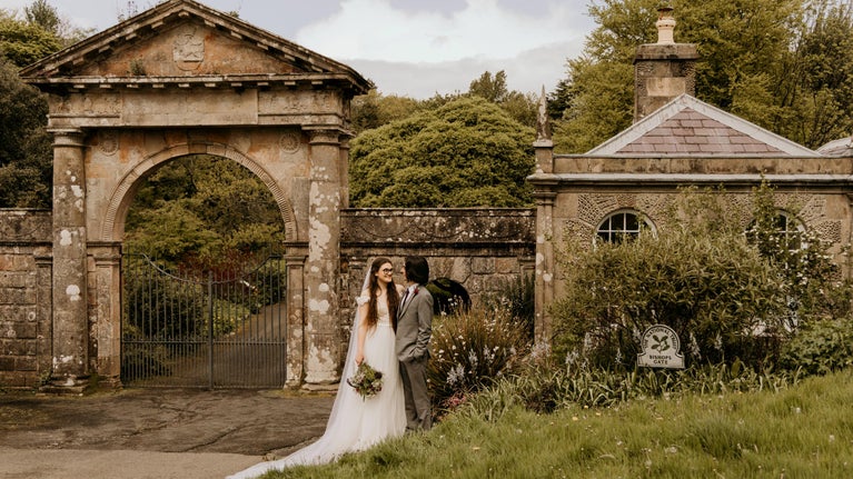 An image of a bride and groom standing outside the Bishop's Gate entrance to Downhill Demesne.